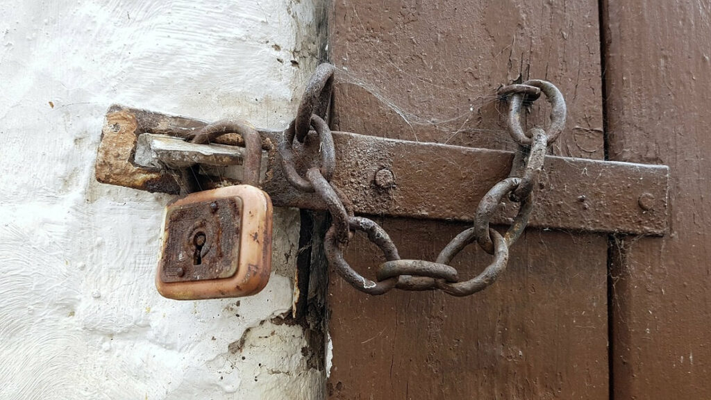 Como manter a segurança em casa quando for viajar? 1 Cadeado trancando a porta de madeira de uma casa