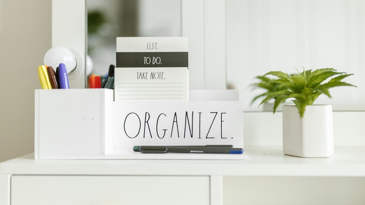 Pequena mesa com espeçho e luzes ao redor, com placa de organização e demais materiais
