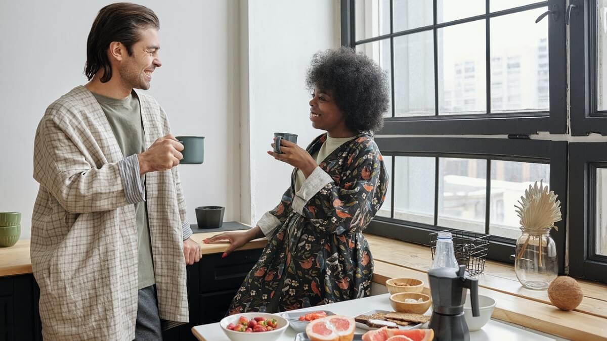 Como decorar um imóvel novo. Casal conversando em uma cozinha, tomando café e ao lado uma mesa com muitas frutas