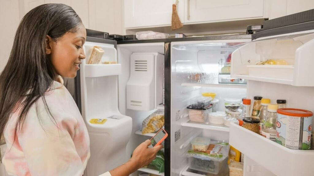 Como tirar cheiro da geladeira: 10 dicas práticas, naturais e econômicas! 1 Mulher vendo em seu celular Como tirar cheiro da geladeira, frente a ela