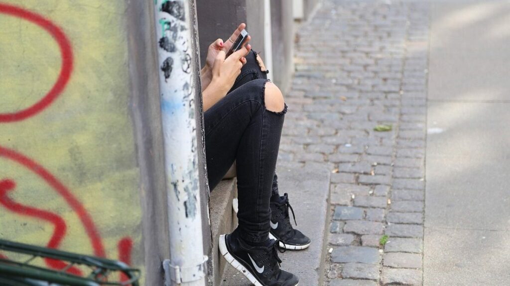 Pessoa sentada no degrau da escada mexendo no celular
