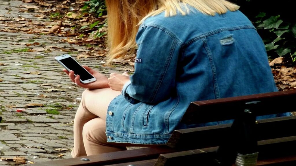 O que significa bv no WhatsApp: Conheça o real significado desta gíria! 2 Garota sentada ao ar livre utilizando o celular.