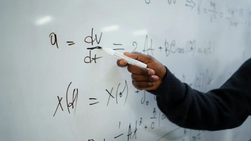 Pessoa segurando um canetão apontando para um quadro cheio de números.
